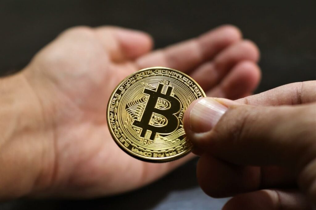 A Golden Bitcoin Being Held by a Mans Hand About to Be Given to Another Person 1 1024x682.jpeg